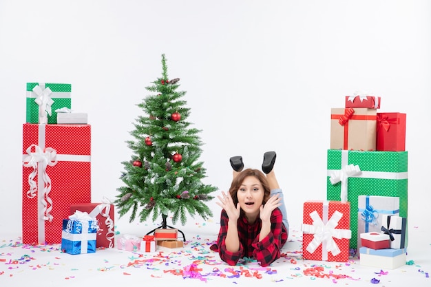 Вид спереди молодая женщина, лежащая вокруг рождественских подарков и праздничной елки на белом столе, рождественский новогодний подарок цвет снега