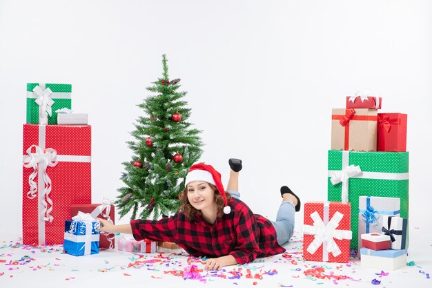 Front view young female laying around christmas presents and little holiday tree on the white background cold woman xmas new year snow