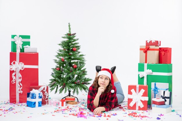 Front view young female laying around christmas presents and little holiday tree on a white background new year cold woman xmas snow