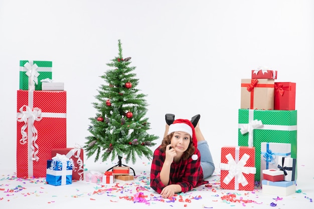 Front view young female laying around christmas presents and little holiday tree on the white background new year cold woman xmas snow