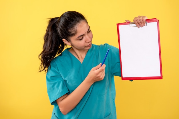 Front view of young female looking at clipboard on yellow wall