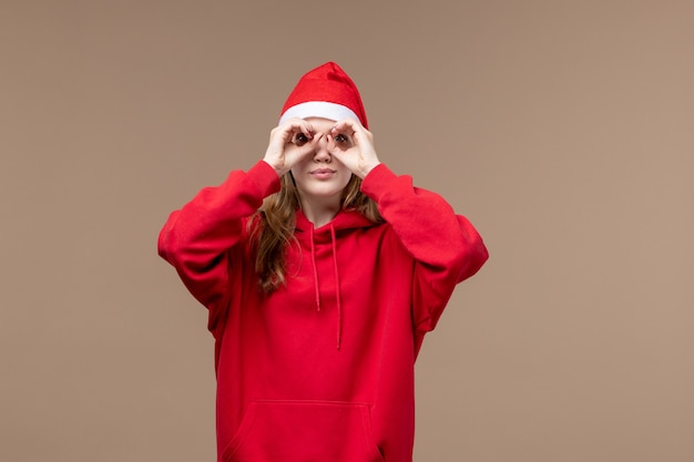 Вид спереди молодая женщина, глядя сквозь пальцы на коричневый фон рождественские эмоции праздник