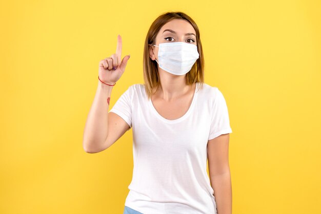 Front view of young female in mask on a yellow wall