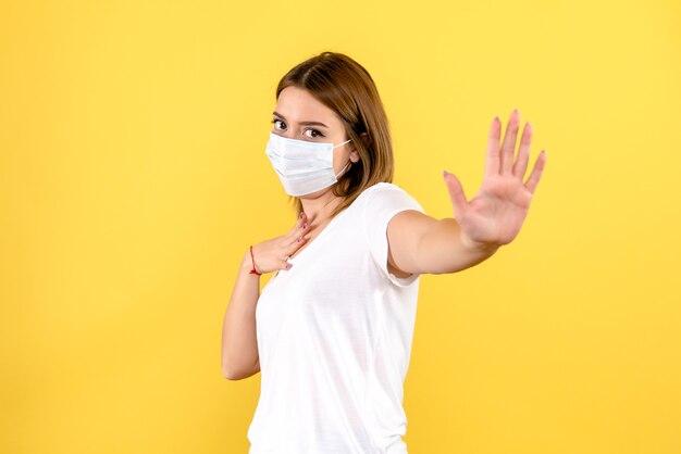 Front view of young female in mask on a yellow wall