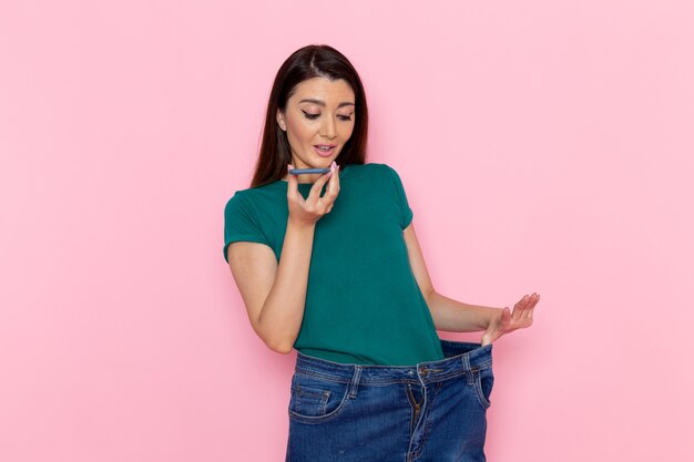 front view young female measuring her waist and talking on the phone on pink wall exercise sport workout athlete waist beauty