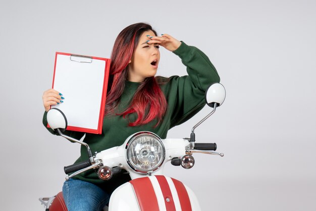 Front view young female on motorcycle holding note for signature on a white wall