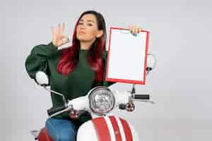 Foto gratuita vista frontale giovane donna sulla moto che tiene nota per la firma sul muro bianco