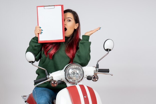 Front view young female on motorcycle holding note for signature on the white wall