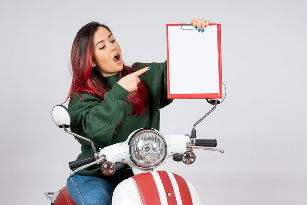 Вид спереди молодая женщина на мотоцикле, держащая записку для подписи на белой стене