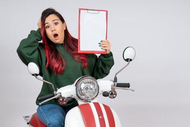 Front view young female on motorcycle holding note for signature on white wall