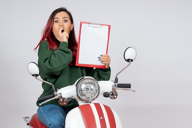 Front view young female on motorcycle holding note for signature on white wall