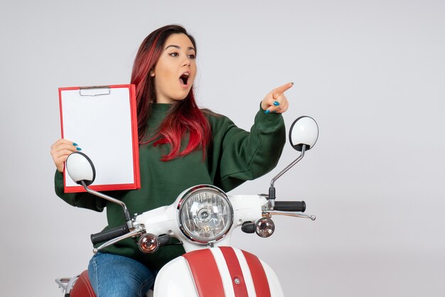 Front view young female on motorcycle holding note for signature on white wall