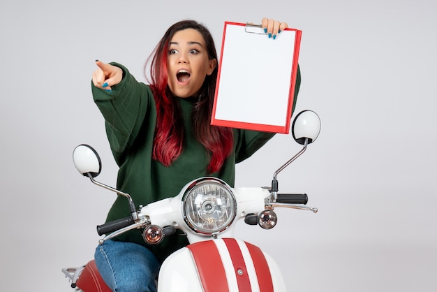 Front view young female on motorcycle holding note for signature on white wall