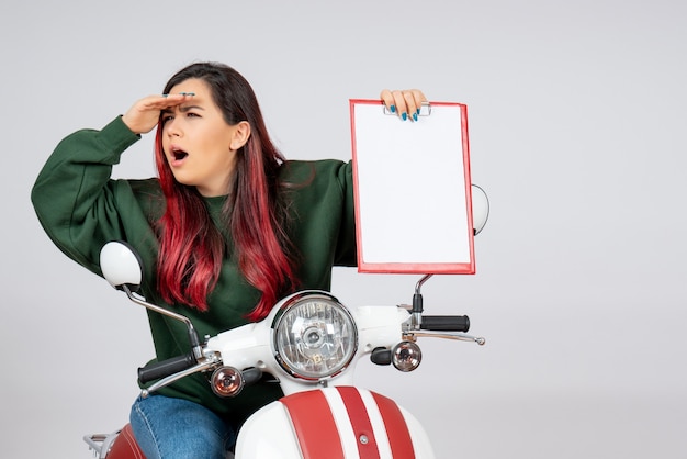 Free photo front view young female on motorcycle holding note for signature on white wall