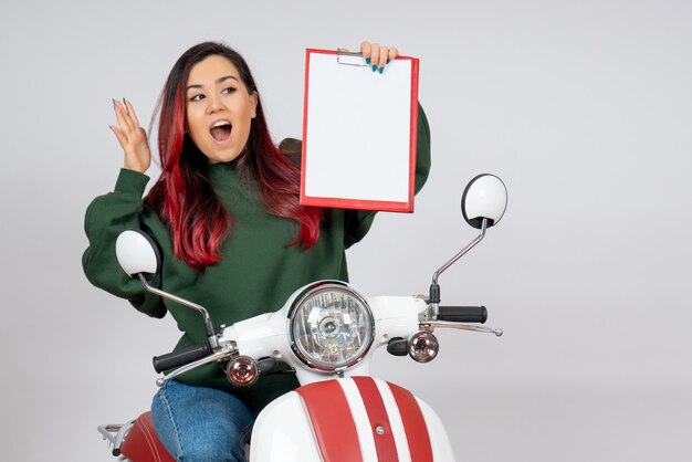 Front view young female on motorcycle holding note for signature on white wall