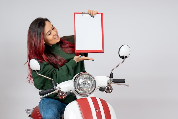 Вид спереди молодая женщина на мотоцикле, держащая записку для подписи на белой стене