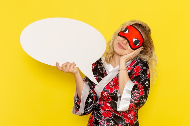 Front view young female in night robe holding huge white sign on light-yellow desk sleep night bed model girl color