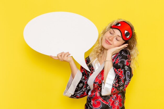 Front view young female in night robe and wearing eye mask holding huge white sign on yellow wall sleep night bed model girl color