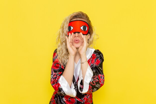 Front view young female in night robe and wearing eye mask preparing to sleep calling out on yellow wall sleep female darkness color night