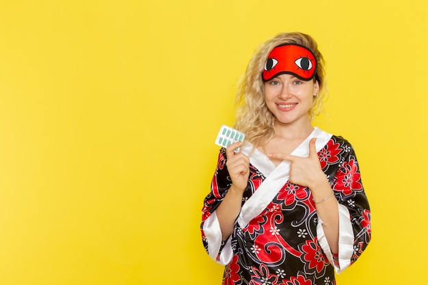 Free photo front view young female in night robe and wearing eye mask preparing to sleep holding pills on the yellow wall sleep female darkness color night