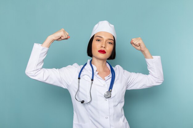 A front view young female nurse in white medical suit and blue stethoscope flexing