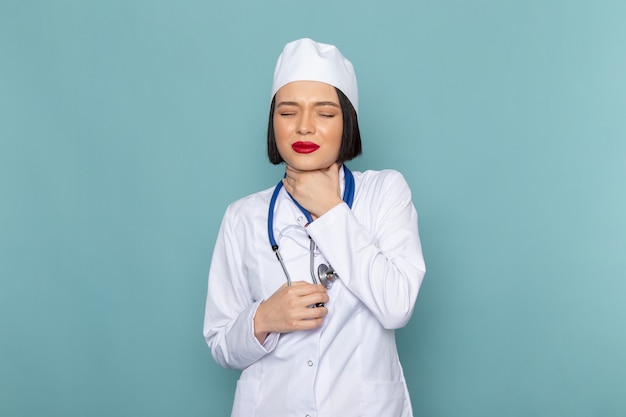 Вид спереди молодая женщина медсестра в белом медицинском костюме и синий стетоскоп с проблемами горла