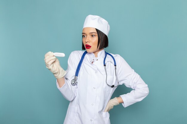 A front view young female nurse in white medical suit and blue stethoscope holding device