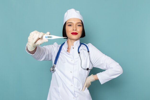 A front view young female nurse in white medical suit and blue stethoscope holding device