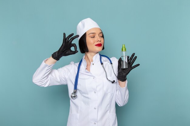 A front view young female nurse in white medical suit and blue stethoscope holding flask
