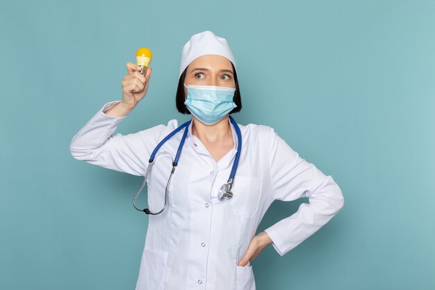 Вид спереди молодая женщина медсестра в белом медицинском костюме и синий стетоскоп, держа лампочку