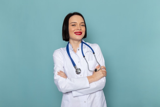 Вид спереди молодая медсестра в белом медицинском костюме и синем стетоскопе позирует на синем столе медицины больнице врач женщина
