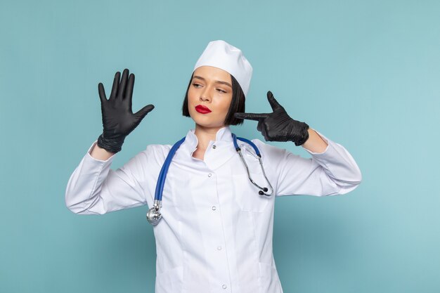 A front view young female nurse in white medical suit and blue stethoscope showing her hand on the blue desk medicine hospital doctor