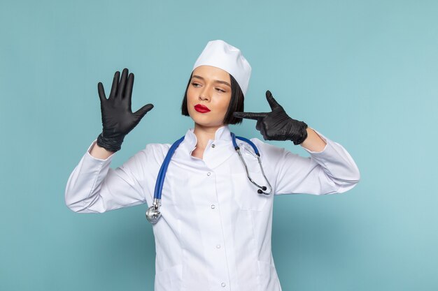 白い医療スーツと青い机の医学病院の医師に彼女の手を示す青い聴診器で正面の若い女性看護師