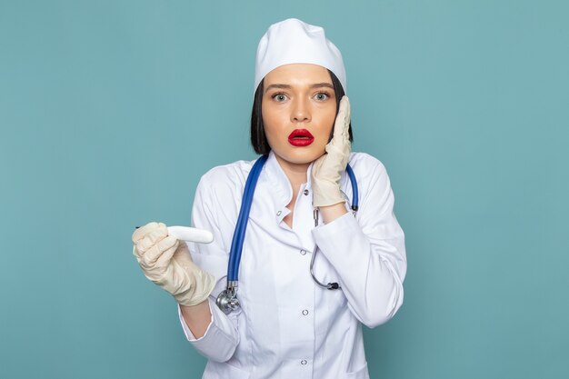 白い医療スーツと青い机医学病院医師スーツに驚いた表情で青い聴診器で正面の若い女性看護師