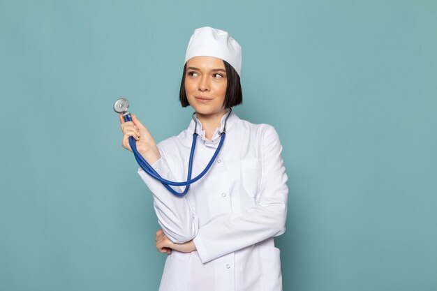 A front view young female nurse in white medical suit and blue stethoscope with thinking expression on the blue desk medicine hospital doctor