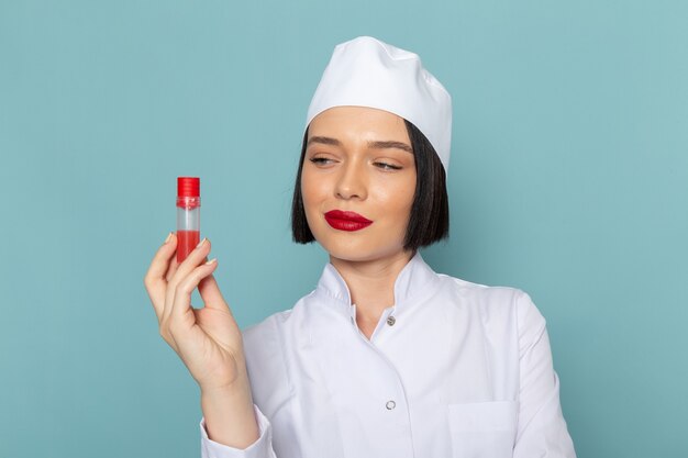 A front view young female nurse in white medical suit holding flask on the blue desk medicine hospital doctor