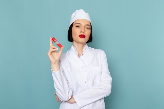 A front view young female nurse in white medical suit holding flask on the blue desk medicine hospital doctor