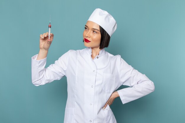 A front view young female nurse in white medical suit holding injection on the blue desk medicine hospital doctor