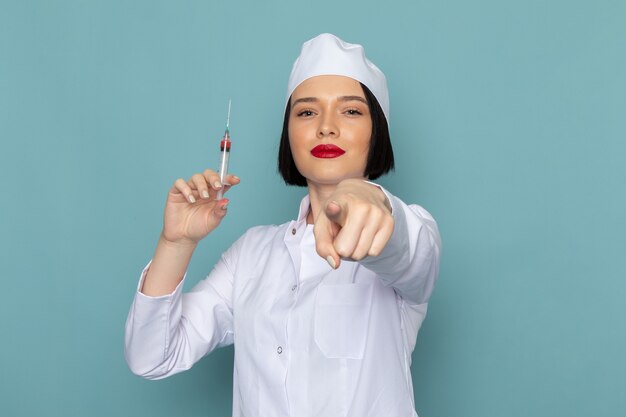 Вид спереди молодая медсестра в белом медицинском костюме с инъекцией на синем столе врача больницы