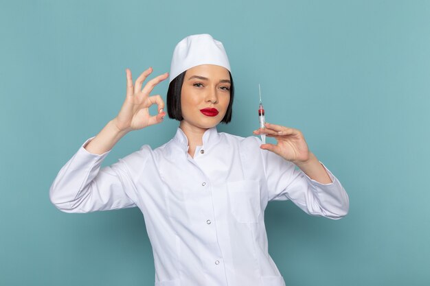 A front view young female nurse in white medical suit holding injection on the blue desk medicine hospital doctor