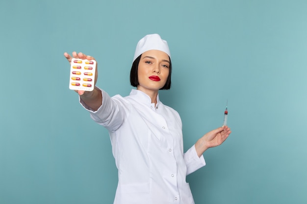 A front view young female nurse in white medical suit holding pills on the blue desk medicine hospital doctor