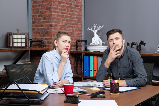 Front view of young female office assistant and her male co-worker sitting at the table discussing one important issue in the office