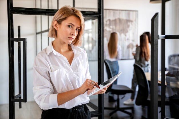 Вид спереди молодая женщина в офисе работает на планшете