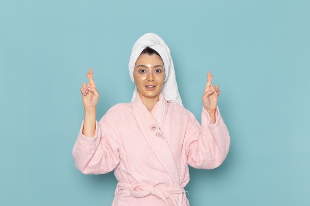 Вид спереди молодая женщина в розовом халате после душа на синей стене, косметическая водяная ванна, крем для душа, ванная комната