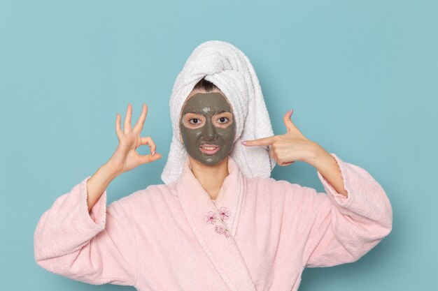 Front view young female in pink bathrobe after shower on the blue wall beauty water bath cream selfcare shower