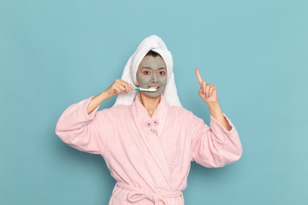 Front view young female in pink bathrobe after shower cleaning her teeth on blue wall cleaning beauty clean water selfcare cream shower