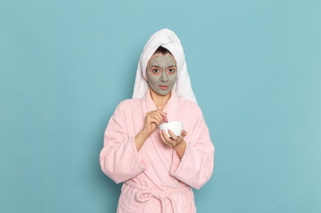 Front view young female in pink bathrobe after shower holding cream on blue wall cleaning beauty clean water selfcare cream shower