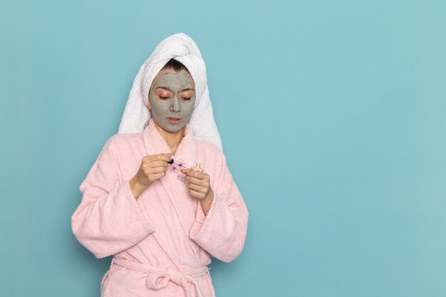 青い机の上のマニキュアを保持しているシャワーの後のピンクのバスローブの正面図若い女性美容ウォータークリームセルフケアシャワー