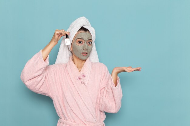 Front view young female in pink bathrobe after shower holding nail polish on blue wall beauty clean water selfcare cream shower