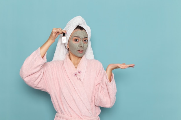 Front view young female in pink bathrobe after shower holding nail polish on blue wall beauty clean water selfcare cream shower